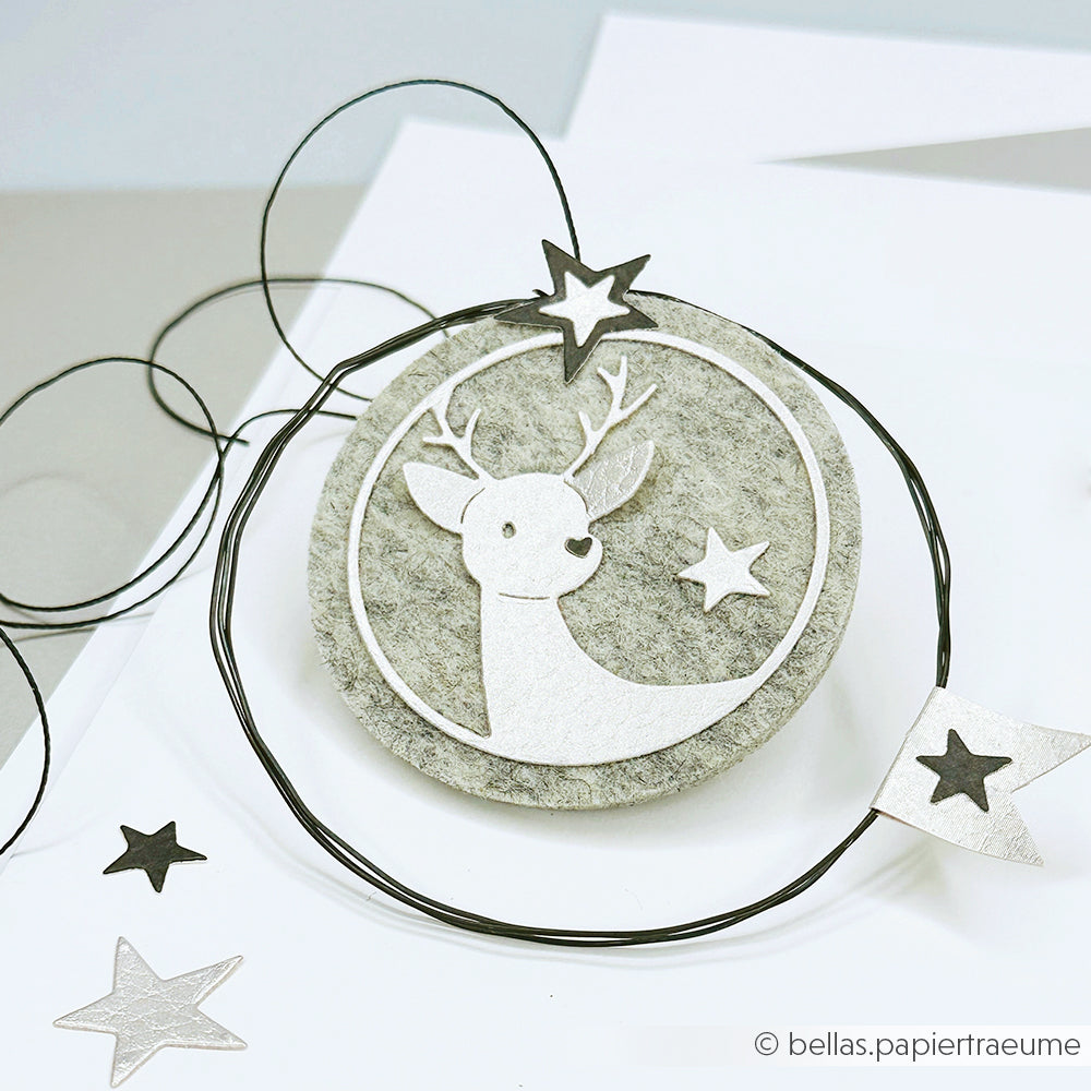 Rundes Filzornament von Alexandra Renke, hergestellt mit Stanzschablone Kreis, mit einem weißen Rentier (Motivstanze Rentier), Sternen und schwarzen Drahtakzenten auf weißem Hintergrund.