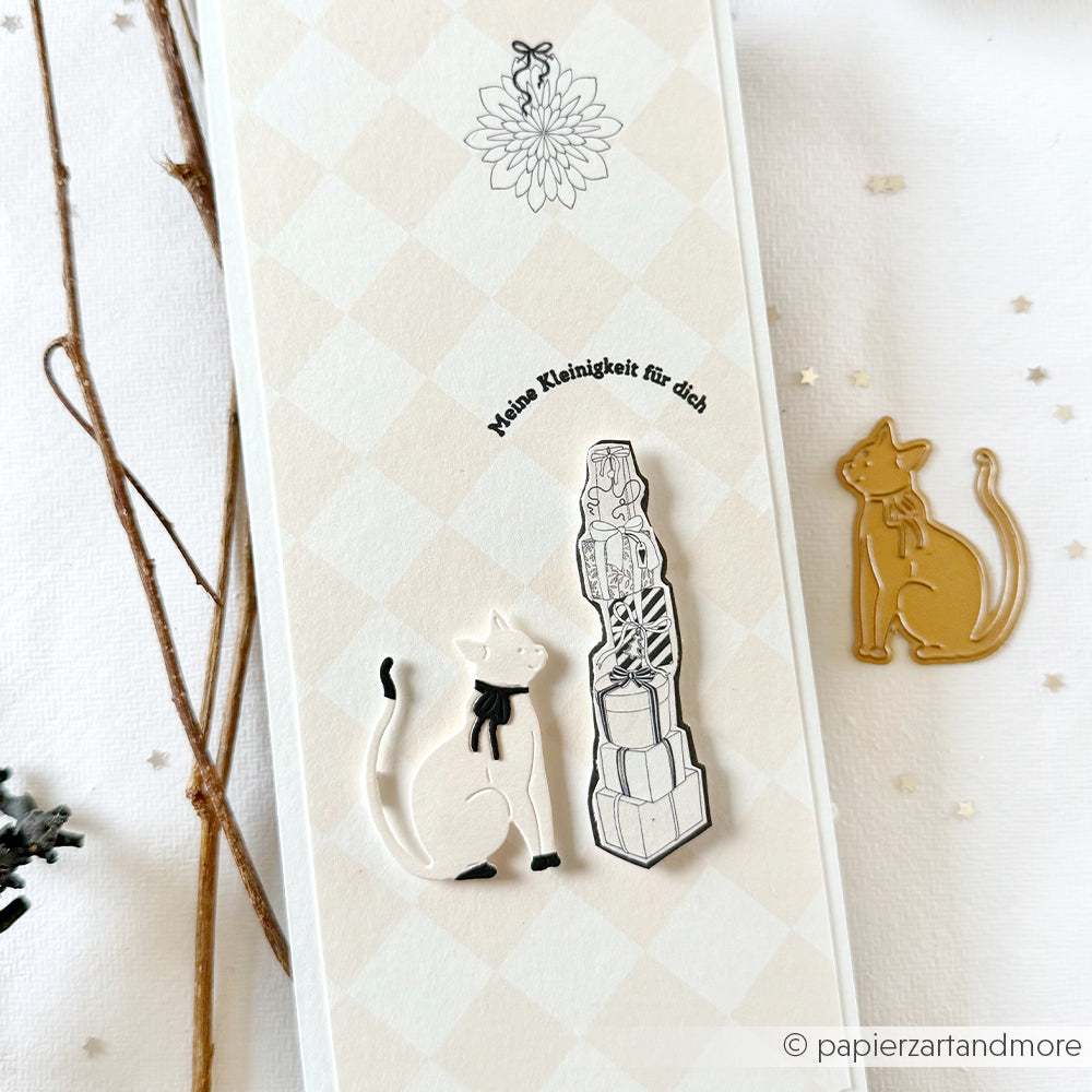 Eine Karte mit einer weißen Katzenillustration aus der Alexandra Renke Motivstanze Neugieriger Katzenfreund, einem Stapel Geschenke und dem Text "Meine Kleinigkeit für dich.