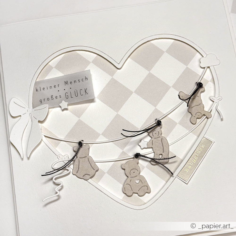 Eine Karte mit einem Herz, Teddybären, die mit dem Alexandra Renke Kleine Bärchen Dies an einer Schnur ausgeschnitten wurden, und dem deutschen Text: kleiner Mensch großes GLÜCK.