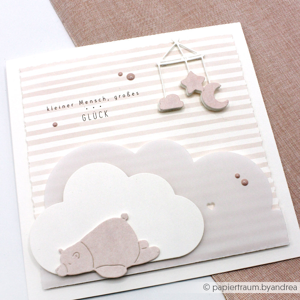 Handgemachte Karte mit Wolken, einem Bären und einem hängenden Mobile; hergestellt mit Alexandra Renke Motivstanze Schlafgefährten und zartem Pastelldesignpapier. Mit deutschem Text für zusätzlichen Charme.
