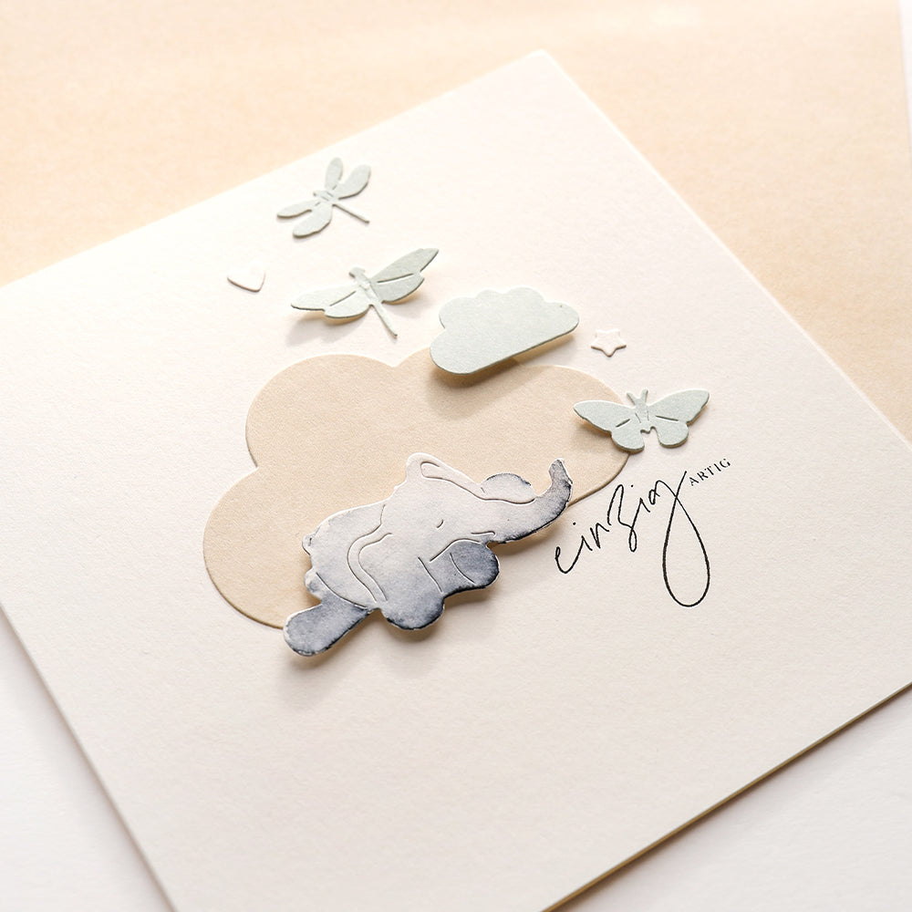 Eine minimalistische Karte von Alexandra Renke, die mit Designpapieren gestaltet wurde und einen Papierelefanten, eine Wolke, Schmetterlinge und Libellen auf einem cremefarbenen Hintergrund zeigt.