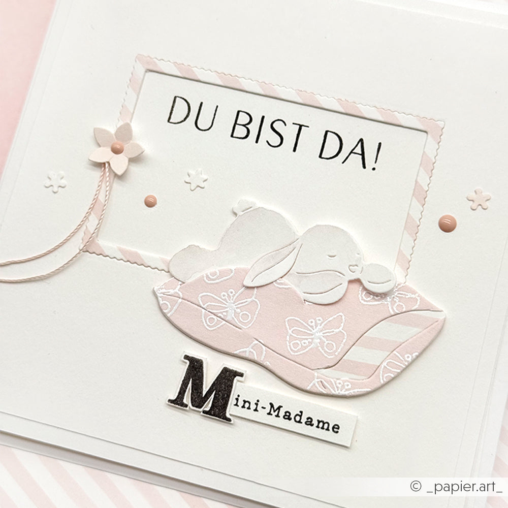 Handgefertigte Karte von Alexandra Renke mit "DU BIST DA!", einem schlafenden Hasen, rosa Akzenten und "Mini-Madame" am unteren Rand, hergestellt mit hochwertigen Designpapieren und charmanten Motivstanze-Details.