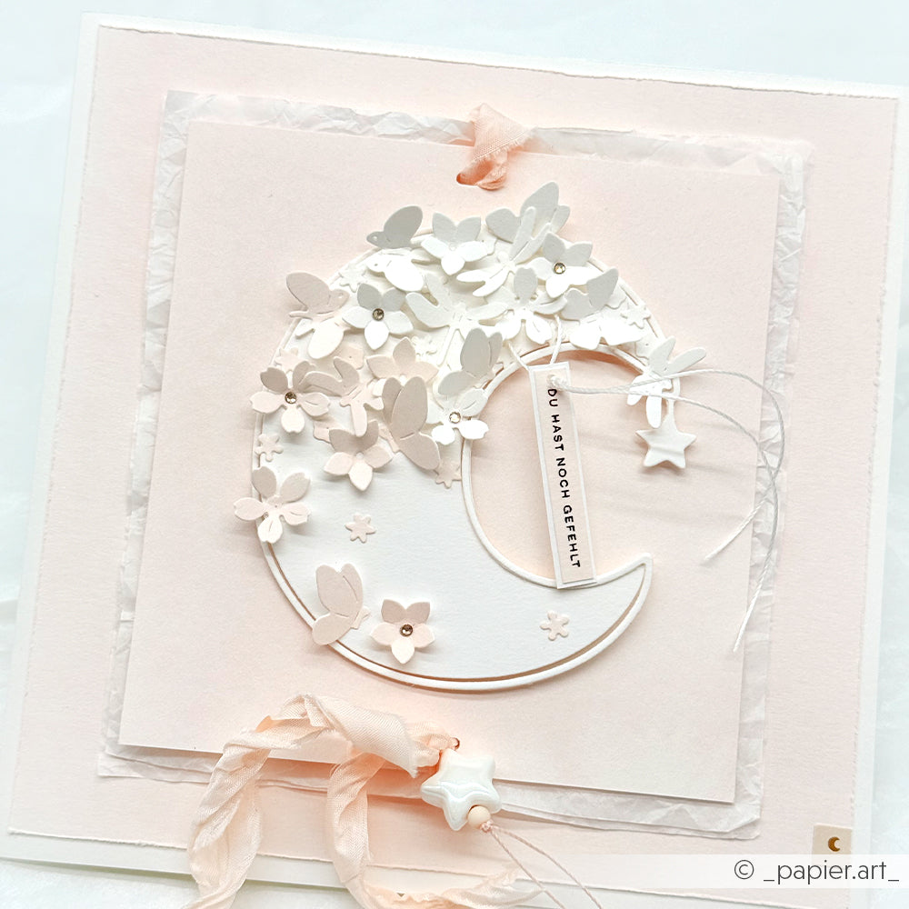 Eine pastellfarbene Karte von Alexandra Renke mit einer Mondsichel, weißen Papierblumen, Sternen und einem Anhänger mit der Aufschrift "You have made of friends", hergestellt mit hochwertigen Designpapieren und detaillierten DieCut Systemen für eine elegante Note.
