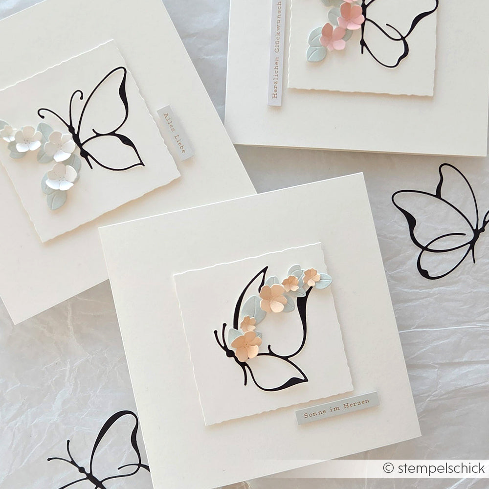 Drei handgefertigte Karten von Alexandra Renke zeigen schwarze Schmetterlingsumrisse, pastellfarbene Papierblumen und weiße Hintergründe, die mit zarten Designpapieren kombiniert werden und so für ein charmantes Finish sorgen.