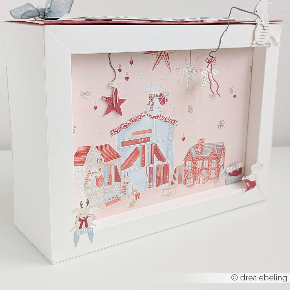 Ein Schattenkasten-Diorama mit einem rosa Winterdorf, Mäusen und Dekorationen von Dackel & Rentier.