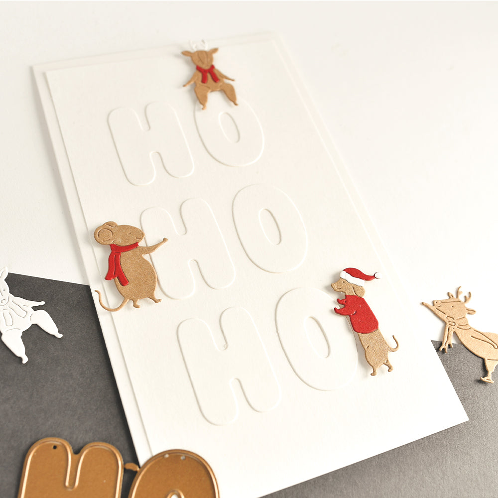 Eine weiße Weihnachtskarte mit geprägtem „HO HO HO“-Schriftzug, verziert mit ausgestanzten Papiertieren in Form von Dackeln und Rentieren.