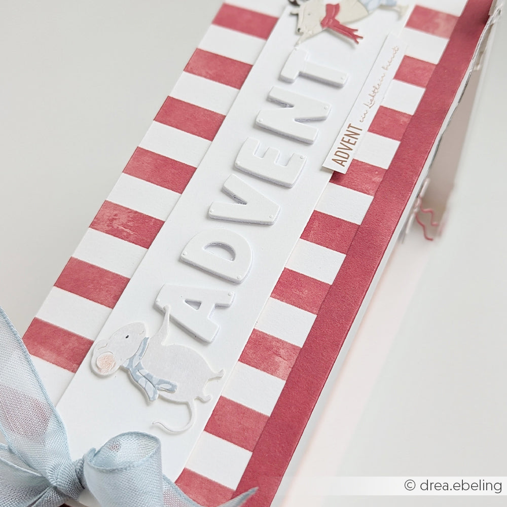 Eine Adventsbox aus rot-weißem Designpapier von Rentier & Maus, verziert mit Mäusen und einer blauen Schleife.