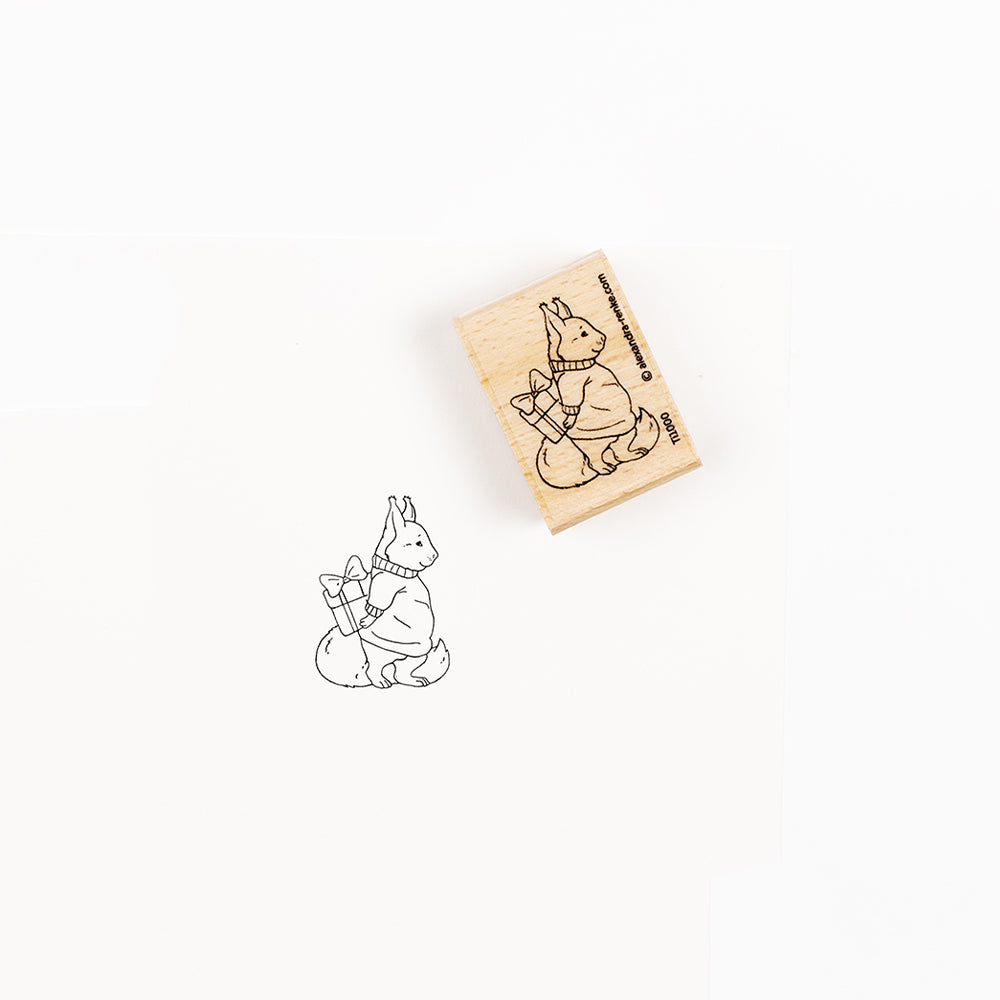 Holzstempel mit dem Motiv eines Eichhörnchens, das ein Geschenk in den Pfoten hält.