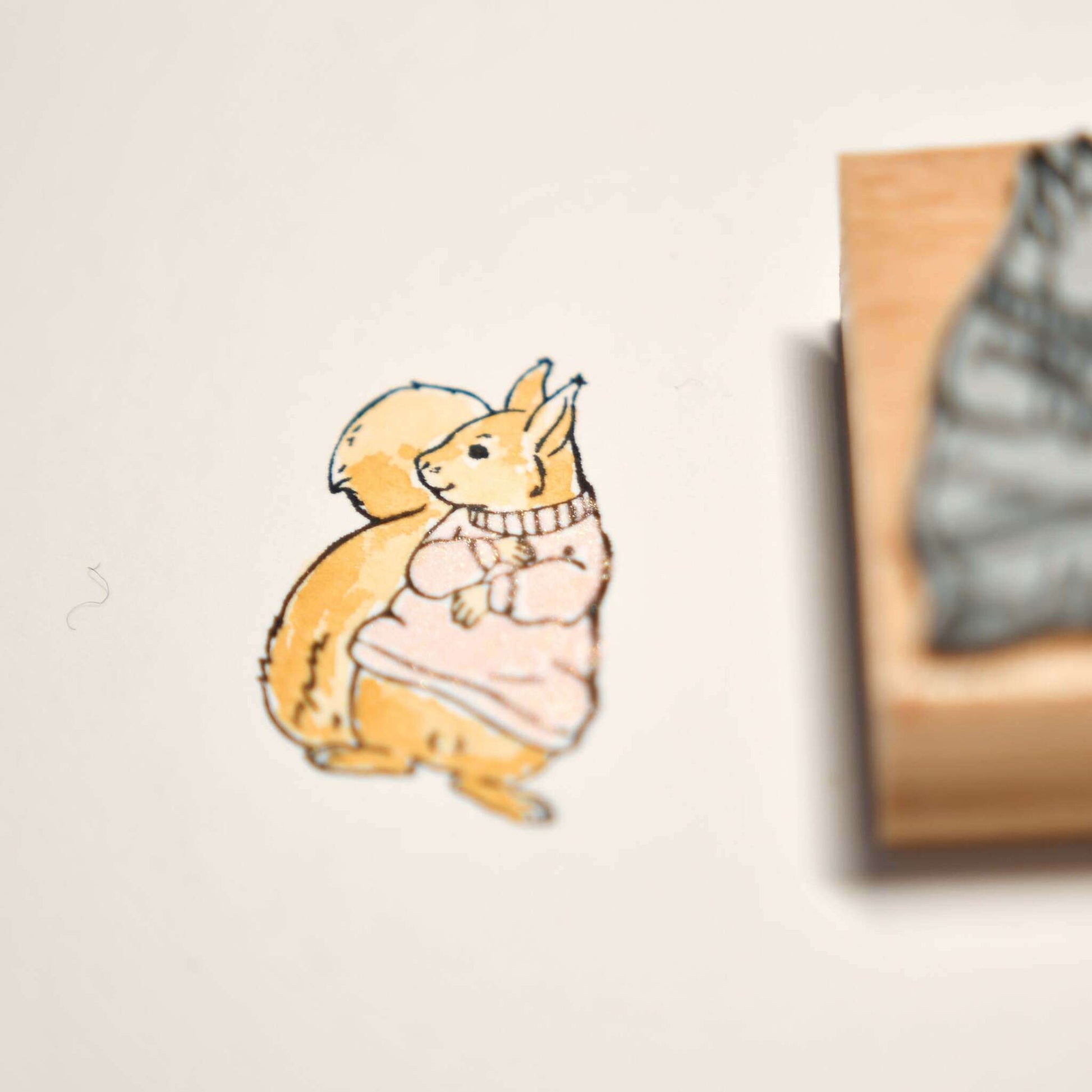 Zeichnung von zwei Kaninchen in kuscheligen Pullovern, die Rücken an Rücken neben einem Alexandra Renke Holzstempel sitzen - die perfekte Inspiration für Ihre Papierprojekte.