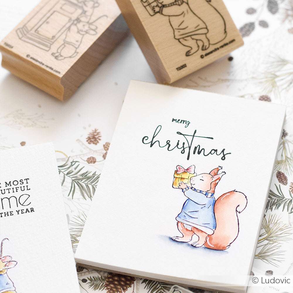 Eine Karte von Alexandra Renke mit einem Eichhörnchen im blauen Kleid, das ein Geschenk in der Hand hält und darüber "Frohe Weihnachten" schreibt - ideal für Fans von Eichhörnchen-Stempeln oder alle, die mit Holzstempeln und Stempelkissen basteln.