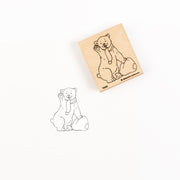 Ein Holzstempel und sein Abdruck, der einen winkenden Bären mit Schal zeigt.