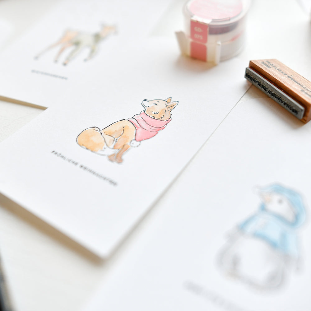 Auf einem Tisch sind illustrierte Tierpostkarten von Alexandra Renke ausgestellt, darunter ein Fuchs mit rosa Schal, daneben liegen Malutensilien und bunte Stempelkissen.