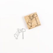 Ein Holzstempel und sein Abdruck, auf dem Hase Hopsi einen Briefkasten überprüft.