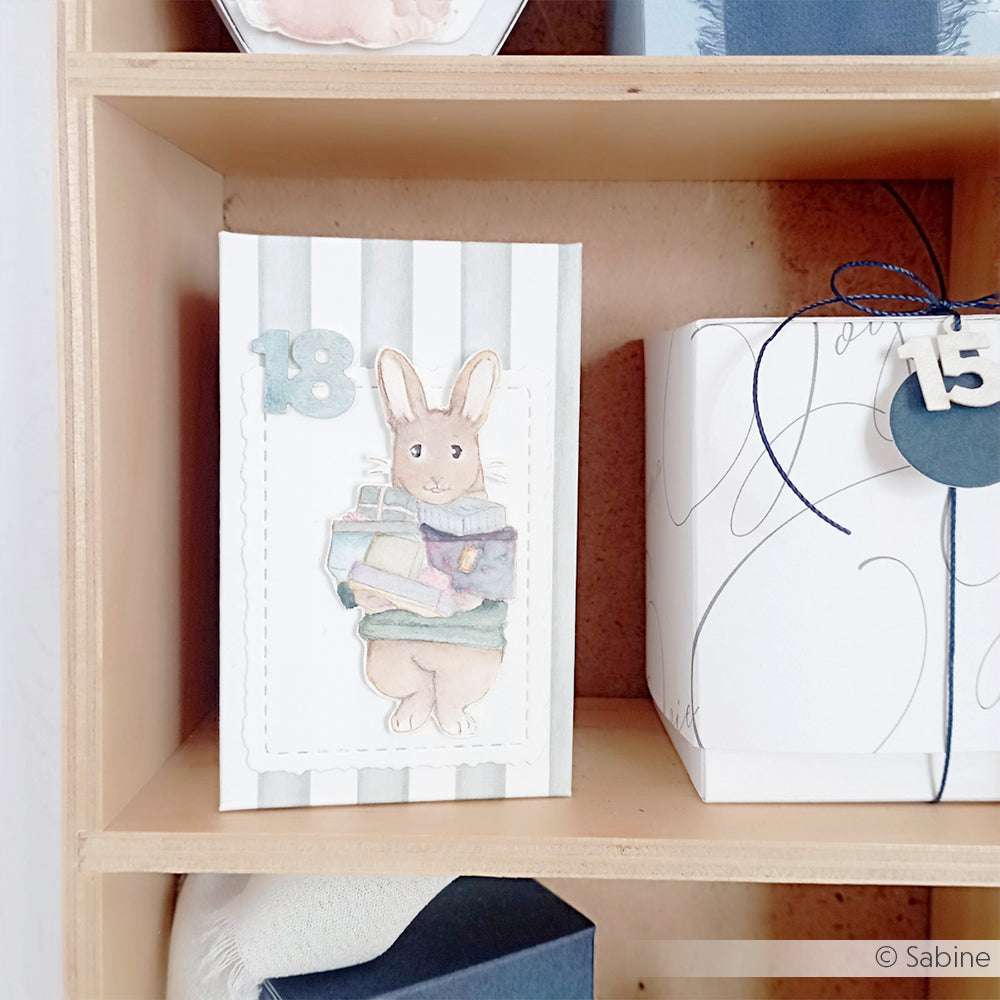 Alexandra Renke Karte mit Hase Henry mit Büchern, Nummer 18 oben, daneben ein Geschenk mit der Nummer 15 - ideal für Papierprojekte oder zum Kombinieren mit Ihren Lieblings-Holzstempel-Motiven.