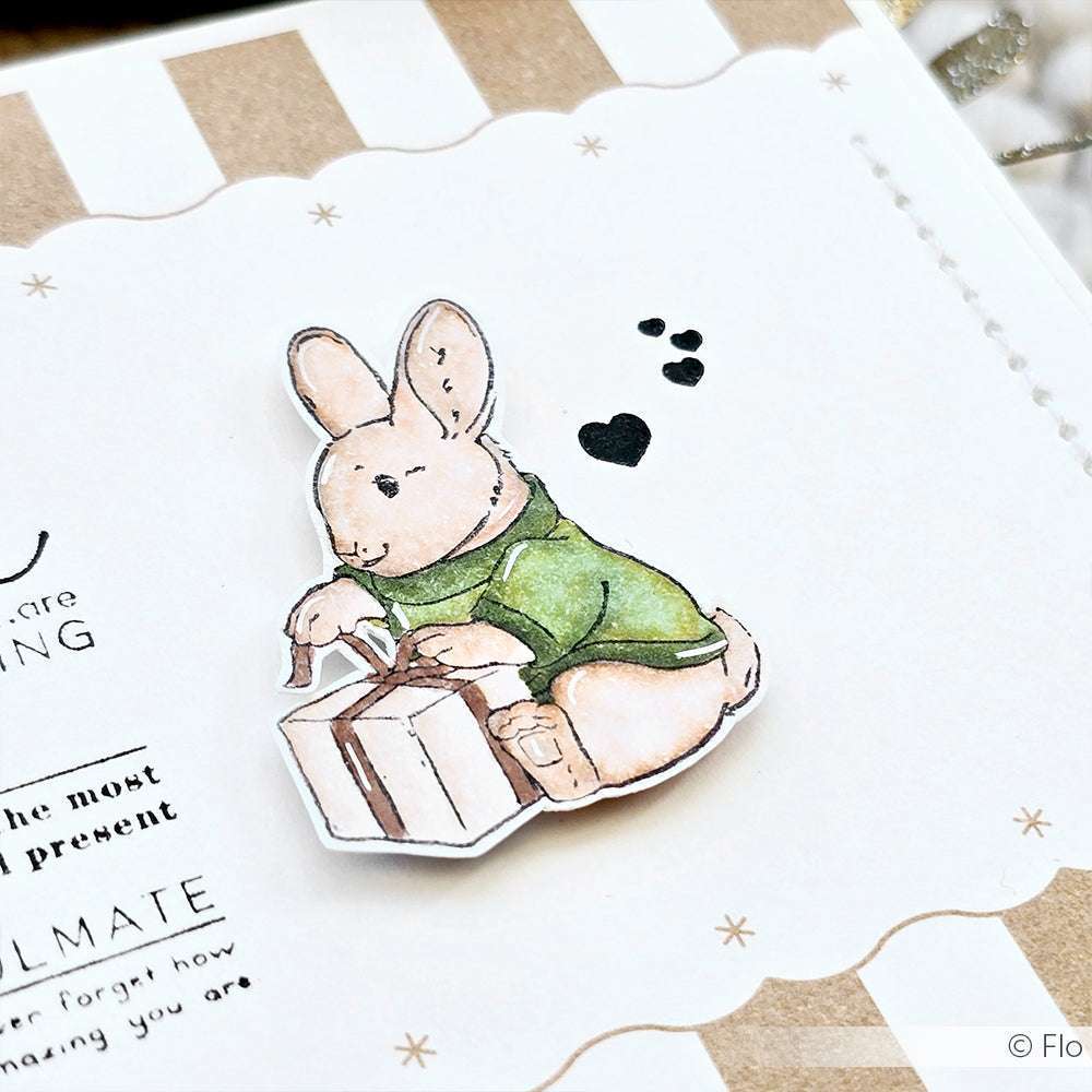 Bezaubernde Alexandra Renke Illustration eines Hasen in einem grünen Pullover, der eine Geschenkbox hält, mit Herz- und Pfotenabdrücken - perfekt als Stempelmotiv für Ihr nächstes Holzstempel-Projekt.