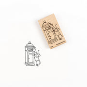 Der Holzstempel Holzstempel und sein Stempelmotiv, das zwei Mäuse zeigt, die einen Brief in einen Briefkasten werfen.