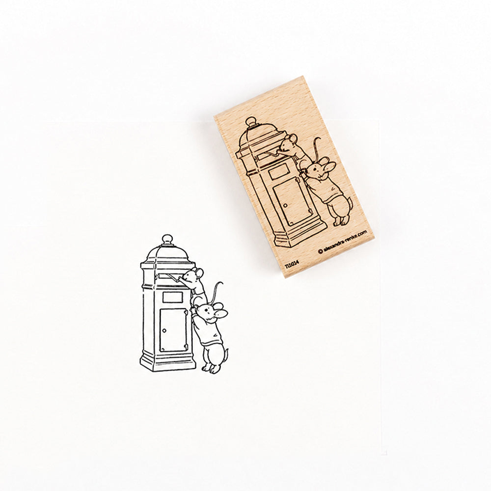 Der Holzstempel Holzstempel und sein Stempelmotiv, das zwei Mäuse zeigt, die einen Brief in einen Briefkasten werfen.