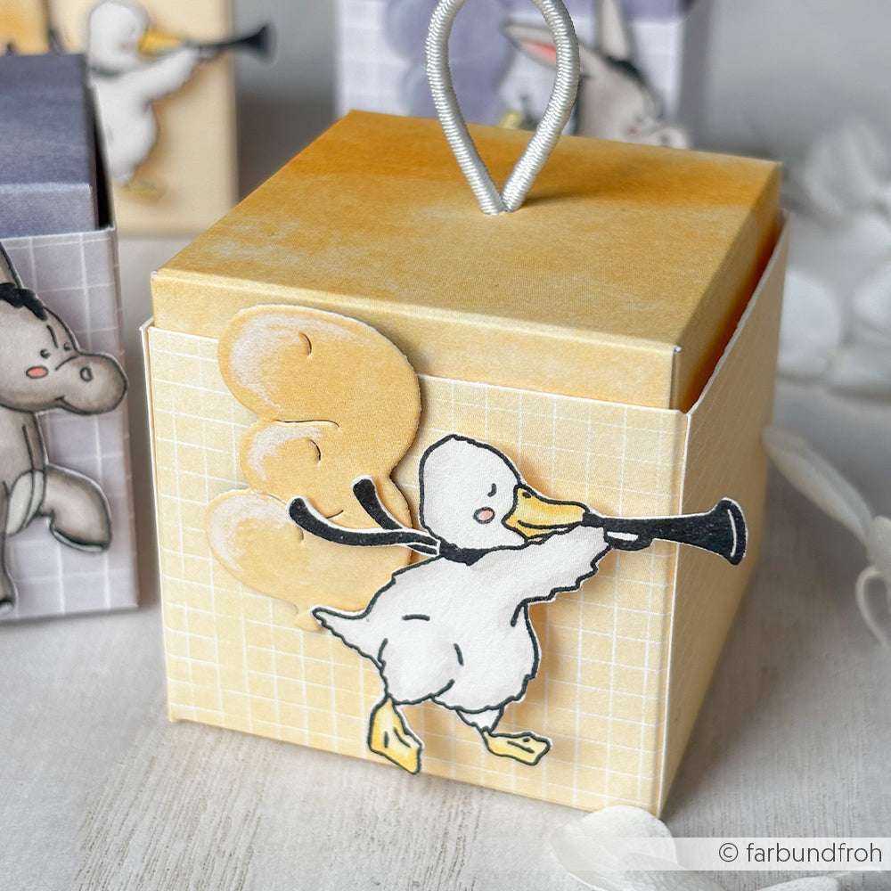 Fröhliche gelbe Geschenkbox von Alexandra Renke mit einer Cartoon-Ente (Trompete & Luftballons) auf dekorativem Hintergrund - ideal zum Kombinieren mit hochwertigem Holz oder Stempelgummi Holzstempel.