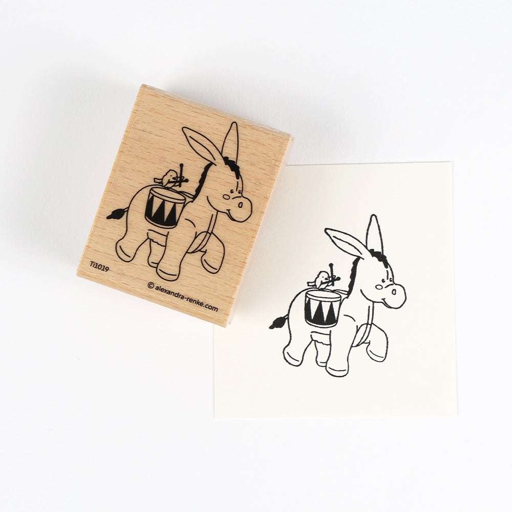 Ein Holzstempel der Marke Alexandra Renke aus hochwertigen Materialien mit einem detailreichen Motiv: Ein Esel, der eine Trommel auf dem Rücken trägt.