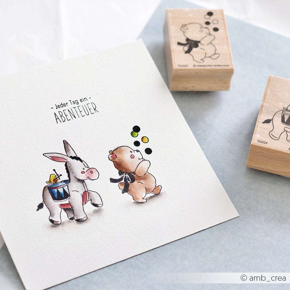 Ein bezauberndes Set von Alexandra Renke: eine Zeichnung eines Esels und ein jonglierendes Bärchen mit Rucksack, dazu zwei Holzstempel im gleichen verspielten Design - ideal für kreative Papierprojekte.