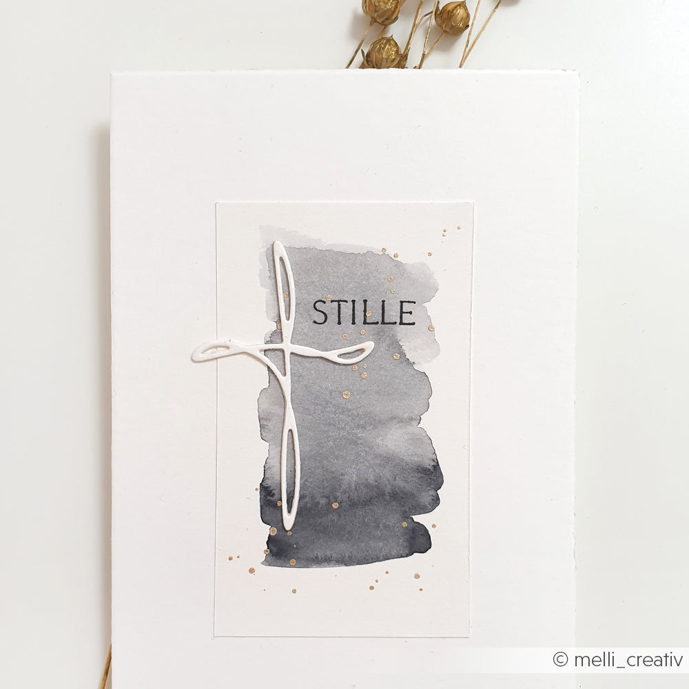 Minimalistische Karte von Alexandra Renke auf hochwertigem Papier, mit einem aquarellierten Hintergrund, einem weißen Kreuz, das mit der Artist Kreuz Stanze ausgestanzt wurde, zarten Goldpunkten und "STILLE" in der Mitte.