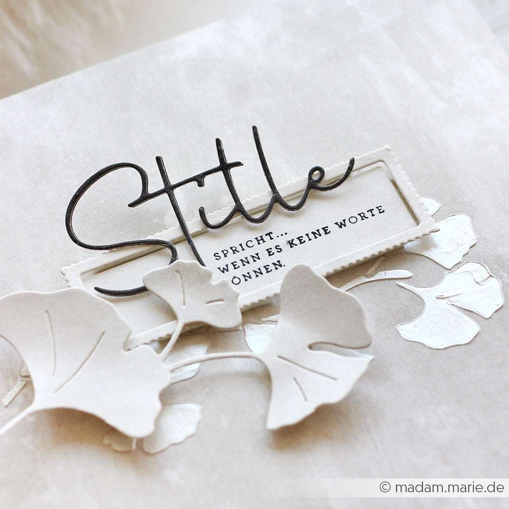 Eine Karte von Alexandra Renke mit Stille und deutschem Text, verziert mit weißen Ginkgoblättern aus Papier, hergestellt mit Stanzsystemen und eleganten Designpapieren.