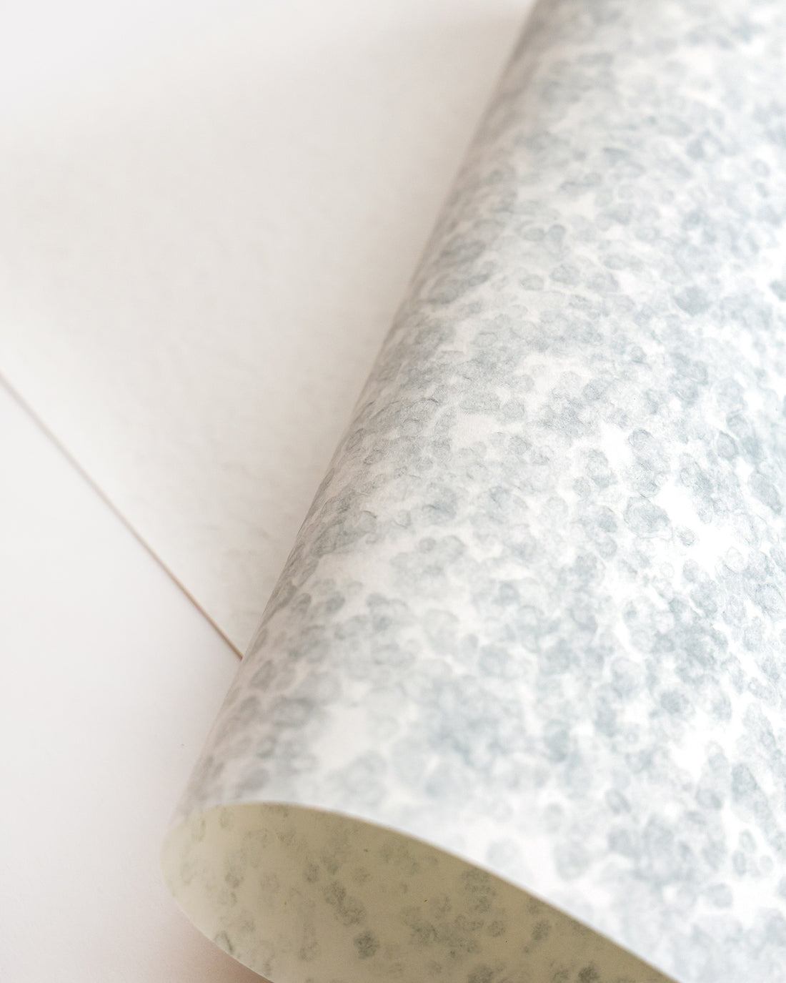 Ein Blatt strukturiertes, gepunktetes weißes und graues Papier, das teilweise auf eine flache weiße Oberfläche gerollt ist.
