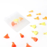Eine Mischung aus kleinen orangefarbenen und gelben Quasten von Alexandra Renke, verteilt auf einer weißen Unterlage, wobei einige in einem durchsichtigen Plastikbeutel verstaut sind – ideal für Buchbindearbeiten oder um Ihren Bastelprojekten ein charmantes Schmuckstück hinzuzufügen.