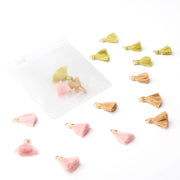 Kleine Quasten in Rosa, Gold und Grün von Alexandra Renke sind verstreut angeordnet, einige davon befinden sich in einem mattierten Plastikbeutel – ein bezauberndes Schmuckstück, das sich perfekt zur Verzierung von Buchbindearbeiten oder kreativen Projekten eignet.