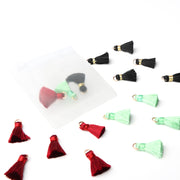 Kleine rote, mintgrüne und schwarze „Alexandra Renke Tasseln“ liegen verstreut neben einem durchsichtigen Plastikbeutel auf einer weißen Fläche – perfekte Akzente für Ihre Papierprojekte und Buchbindearbeiten.