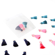 Die „Mini Tasseln Mix“ in Blau, Rosa und Marineblau von Alexandra Renke sind auf einem weißen Untergrund verstreut – einige davon befinden sich als charmantes Schmuckstück in einem kleinen durchsichtigen Beutel. Perfekt für Buchbindearbeiten und kreative Projekte!.