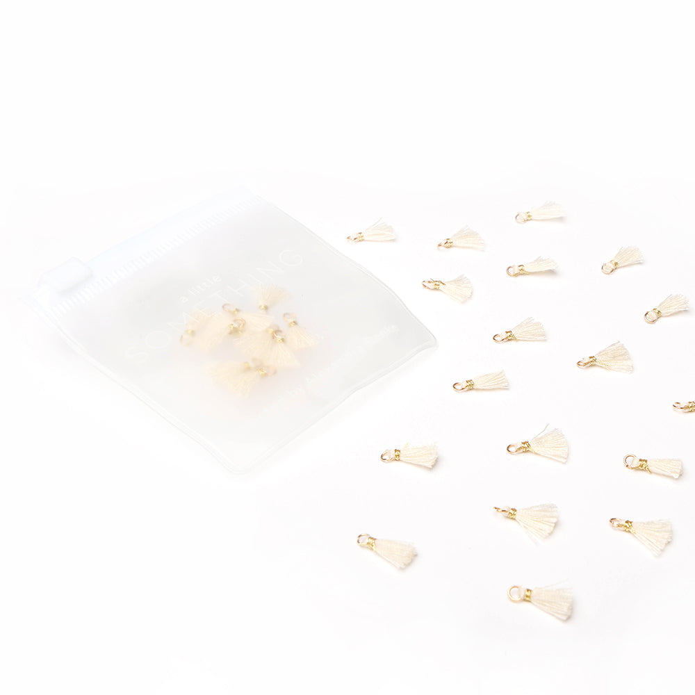 Kleine Tasseln Ivory mit goldenen Schlaufen von Alexandra Renke, einige verstreut und einige in einem durchsichtigen Beutel mit Reißverschluss - perfekte Akzente für Bucheinbände oder zarte Schmuckstücke.