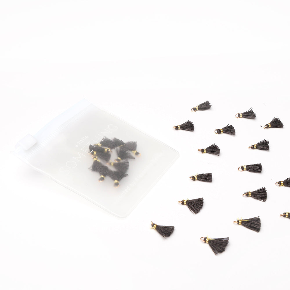 Kleine Tasseln Tiefschwarz von Alexandra Renke mit goldenen Spitzen sind neben einer gefrosteten Reißverschlusstasche auf einer weißen Fläche verstreut - ideal für Schmuck selbst machen oder kreative Buchbindearbeiten.