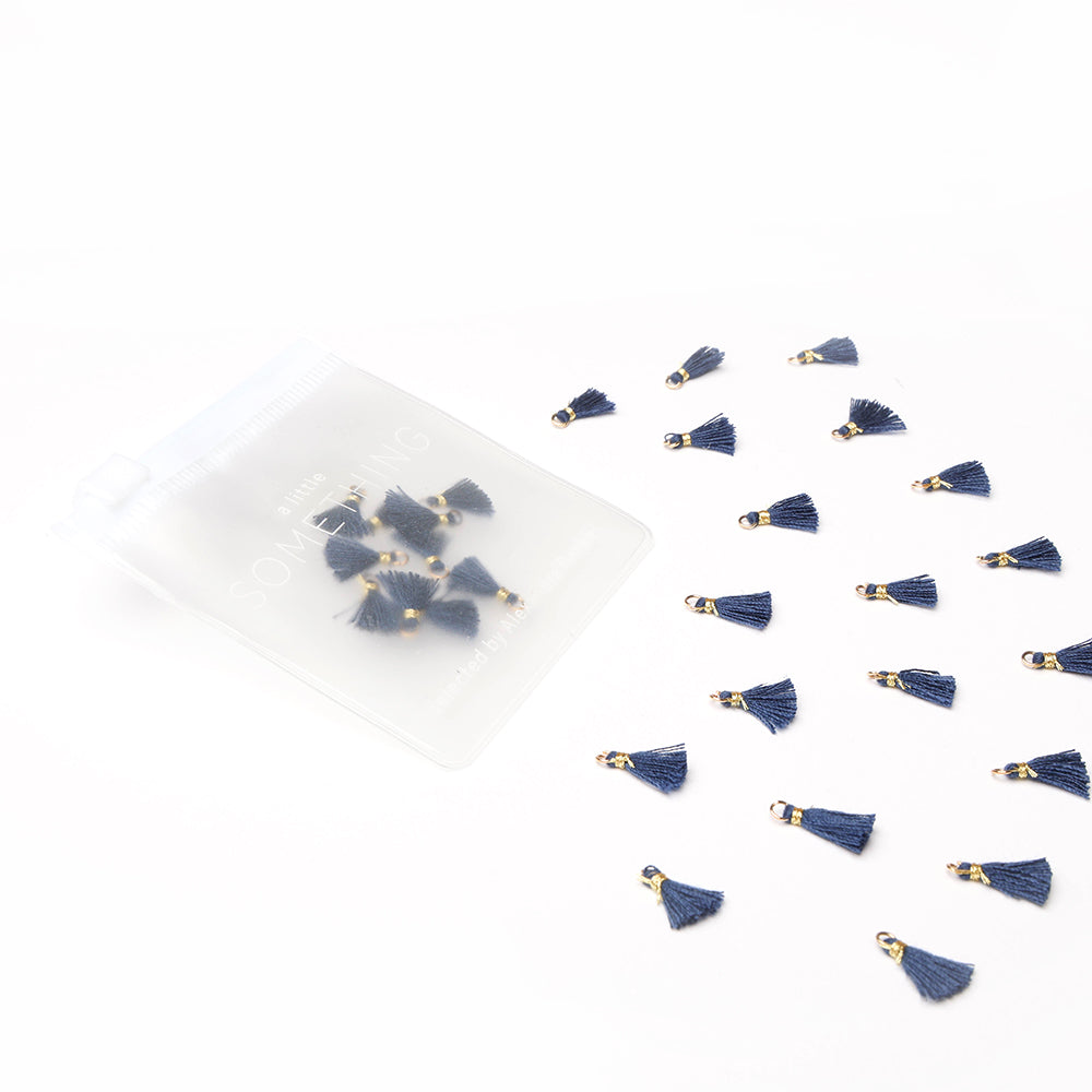 Kleine marineblaue Quasten von Alexandra Renke (Tasseln Königsblau) verstreut auf Weiß, einige in einem durchsichtigen Beutel - perfekt für Buchbindearbeiten oder Schmuck selber machen.