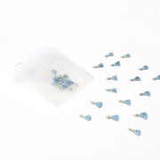 Die kleinen blauen Quastenanhänger von Alexandra Renke, die sich perfekt für Buchbindearbeiten oder als einzigartige Schmuckstücke eignen, werden neben einem durchsichtigen Beutel auf weißem Hintergrund präsentiert.