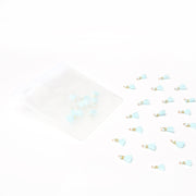 Kleine blaue Quastenanhänger von Alexandra Renke sind verstreut, mit mehreren in einem durchsichtigen Reißverschlussbeutel auf weißem Hintergrund - ideal für Buchbindearbeiten oder als einzigartiges Schmuckstück.