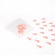 Kleine rosafarbene Quasten von Alexandra Renke, verstreut neben einer transparenten Reißverschlusstasche auf weißem Hintergrund - perfekt als Schmuckstücke oder für Buchbindungsprojekte.