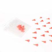 Kleine korallenfarbene Tasseln von Alexandra Renke verstreut neben einem durchscheinenden Beutel auf weißem Grund - ideal für Buchbindearbeiten oder als einzigartiges Schmuckstück.