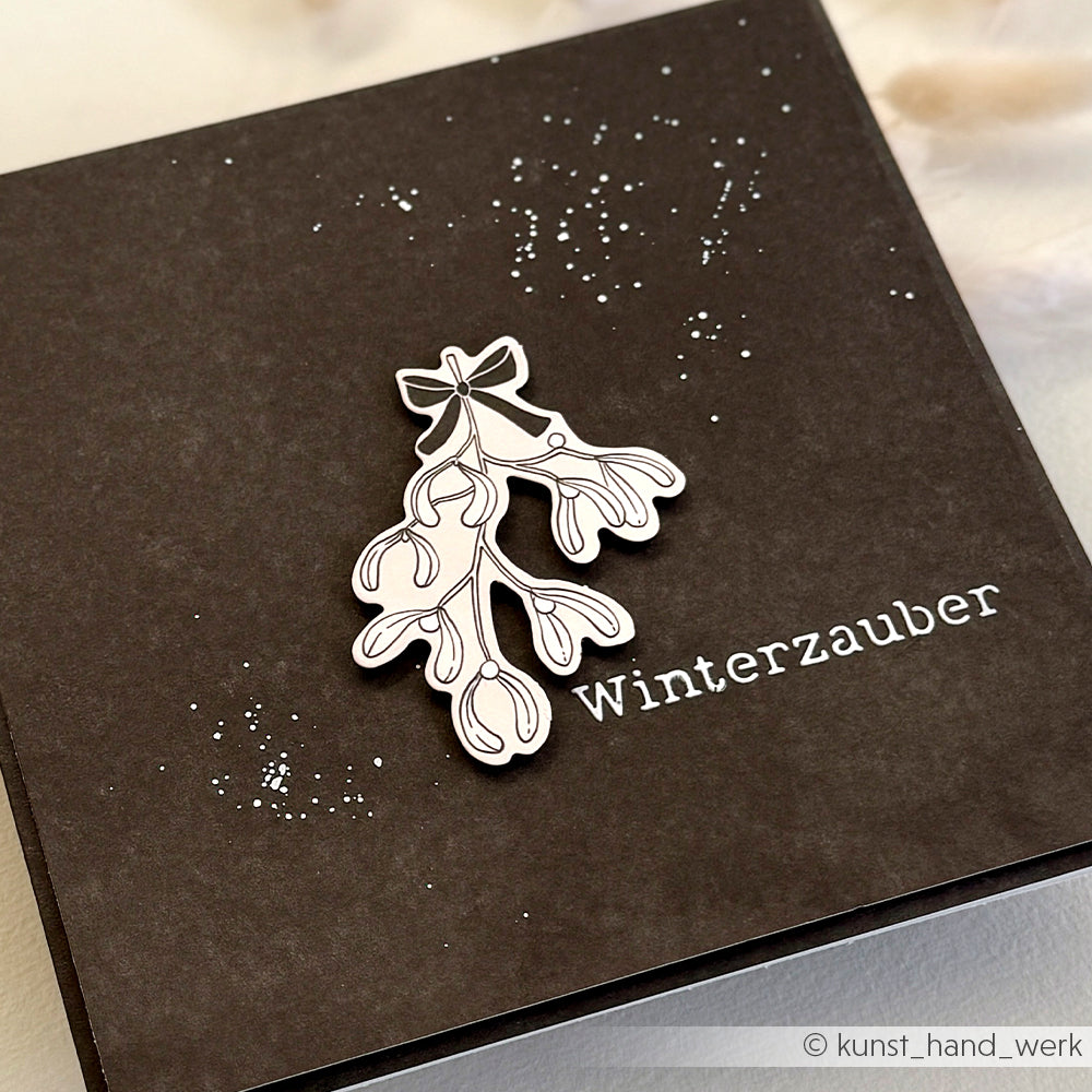 Braune Karte mit weißer Mistelillustration, gestreuten Punkten und "Winterzauber" in Weiß - ideal für Papierprojekte oder als Inspiration für Alexandra Renke Stencil Weihnachtszeit Schablonen.