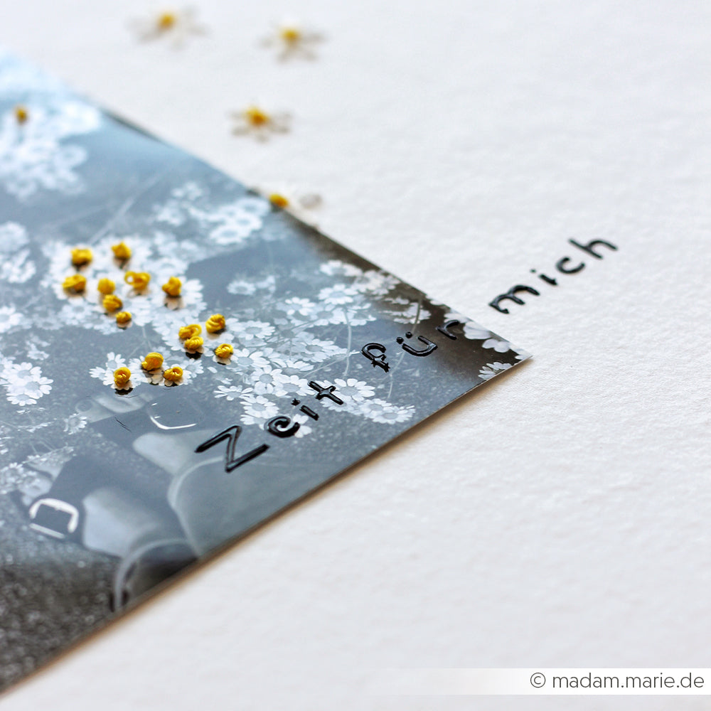 Schwarz-Weiß-Foto mit Blumen und dem Schriftzug „Zeit für mich“ auf weißem Hintergrund, dazwischen verstreute kleine gelbe Knospen – die perfekte Inspiration für Schablonen-Papierprojekte. Diese Szene strahlt eine Ruhe aus, die ideal ist, um mit deiner liebsten wiederverwendbaren Schablone, wie zum Beispiel der Schablone „Kaffeeglück“, zu basteln.