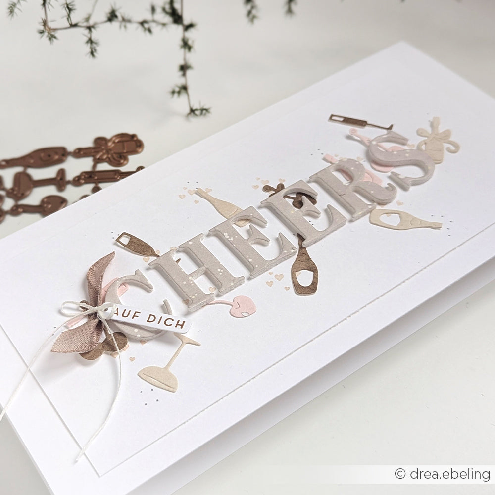 Handgemachte Karte von Alexandra Renke mit "CHEERS" mit Motivstanze Serifen Alphabet, Flaschen- und Glasausschnitten, Designpapieren und einem kleinen "AUF DICH"-Anhänger.