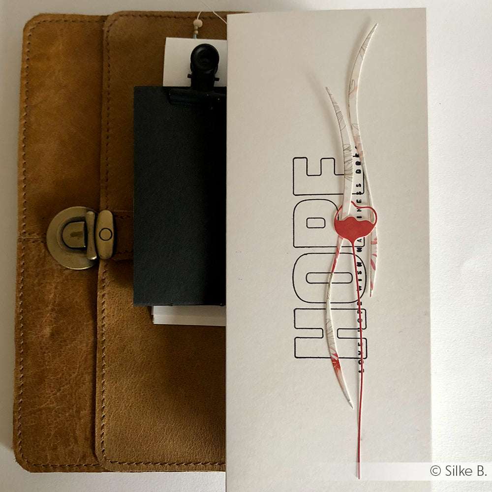 Weiße Karte mit dem Text HOPE und einem abstrakten rot-weißen Muster auf der Oberseite, das auf einem braunen Leder-Organizer ruht. Von Alexandra Renke, perfekt für die Präsentation Ihrer Lieblings-Stempel oder Photopolymer-Stempel-Designs.