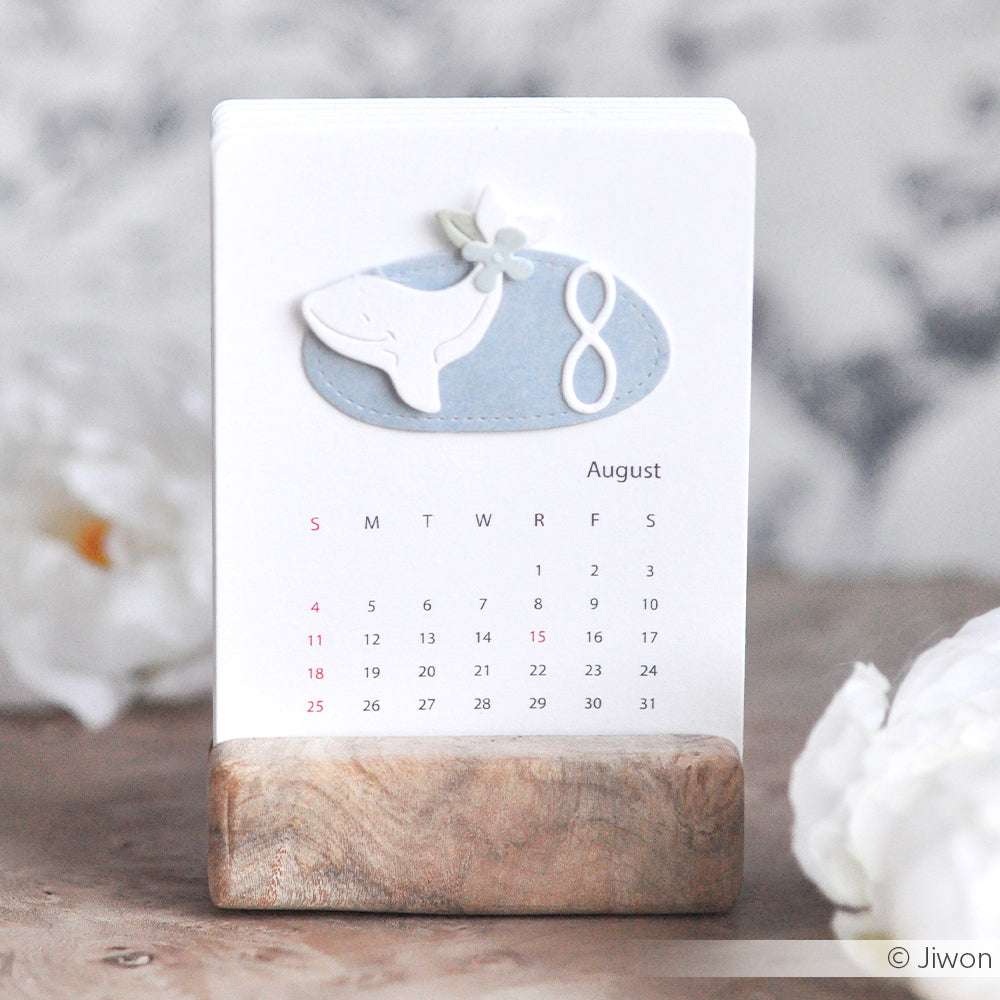 Der August-Tischkalender von Alexandra Renke zeigt eine Wal- und Blumenillustration in einem Holzhalter - ideal für Fans einzigartiger Designs oder für diejenigen, die Stanzsysteme zur kreativen Inspiration nutzen.