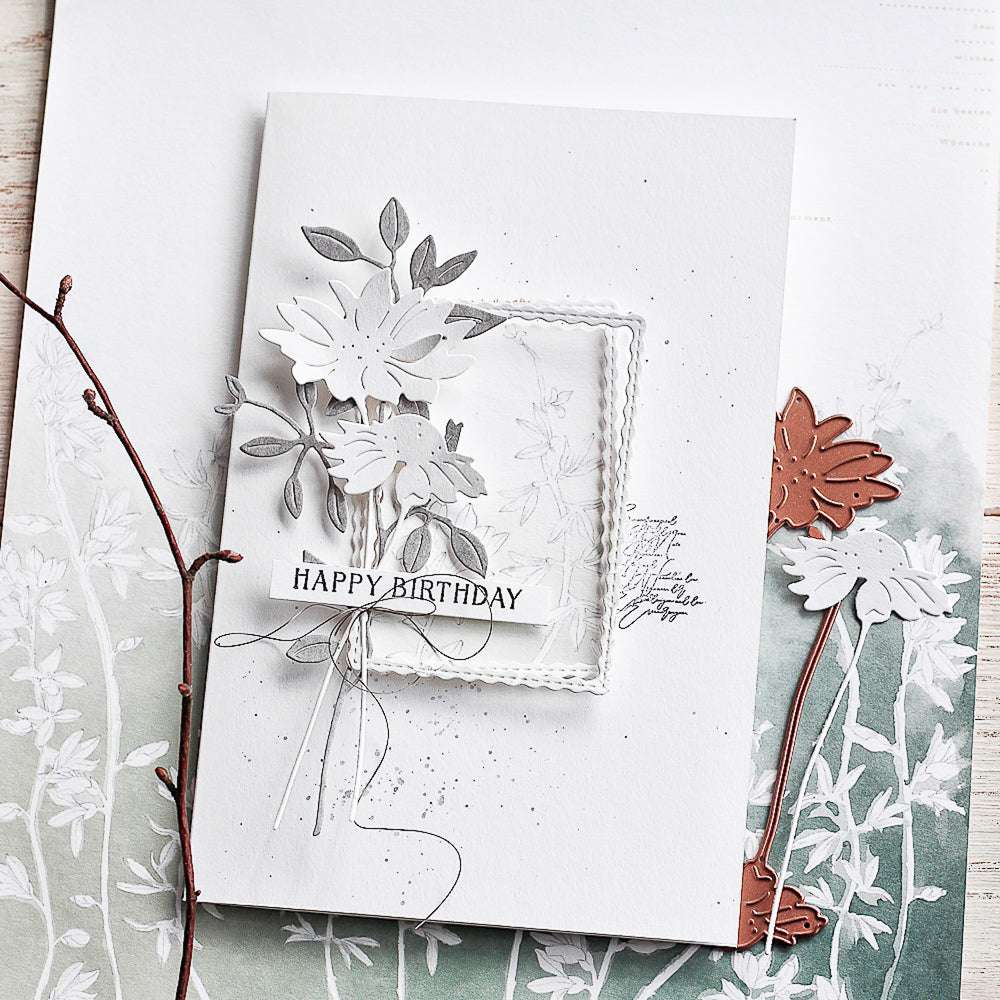 Eine handgefertigte Happy Birthday Karte mit geschichteten Papierblumen, die mit der Alexandra Renke Motivstanze Margeriten-Paar in neutralen Tönen hergestellt wurden, abgeschlossen mit dekorativer Schnur.