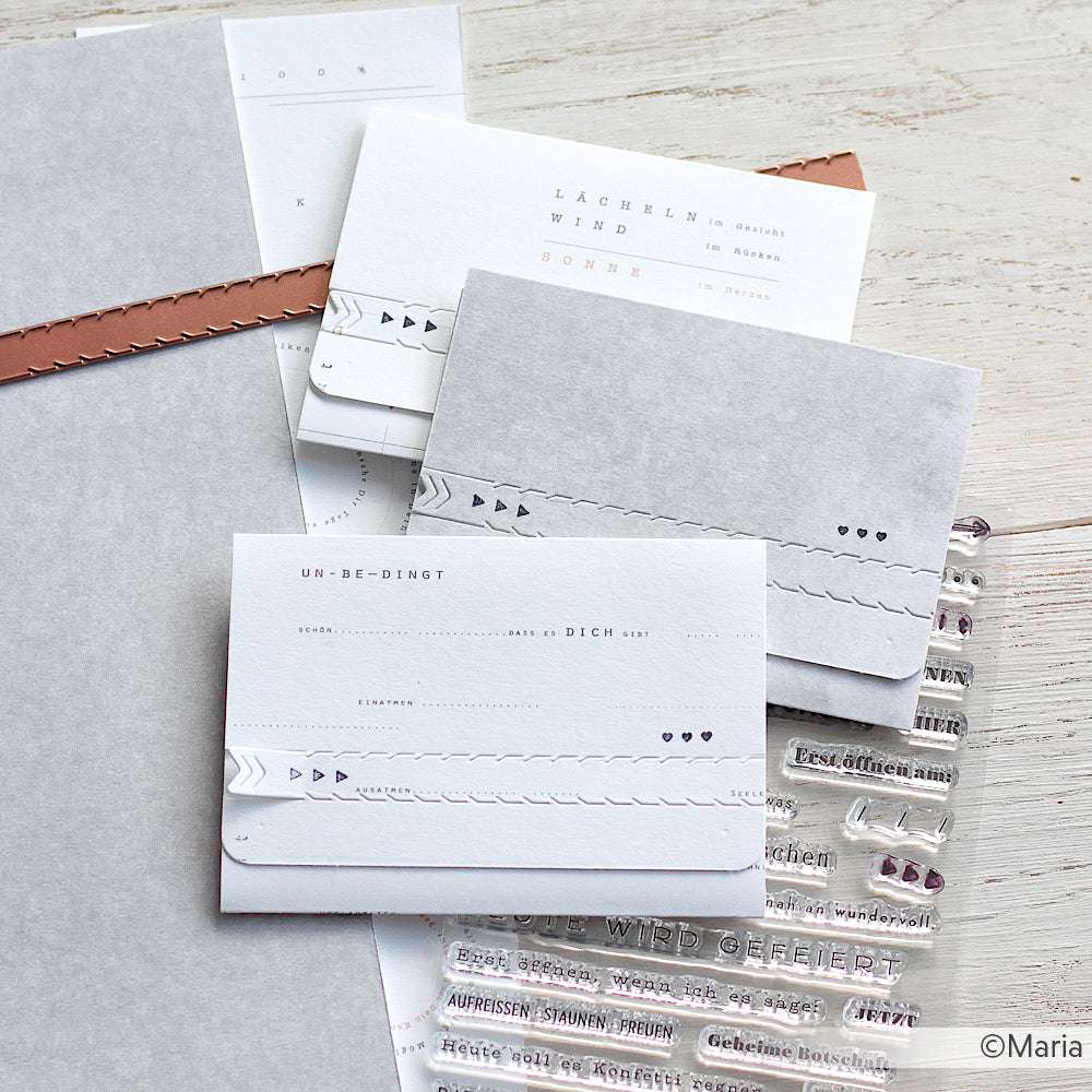 Minimalistische Grußkarten von Alexandra Renke mit geprägten Motiven und deutschem Text liegen auf einer hellen Holzoberfläche, präzise gefertigt mit Motivstanze Abriss-Streifen und hochwertigen Designpapieren.