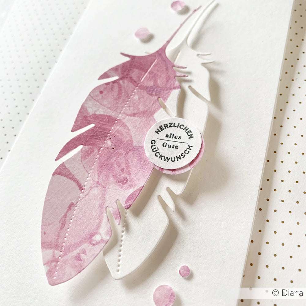 Handgefertigte Karte von Alexandra Renke mit übereinanderliegenden rosa und weißen Federausschnitten, einer deutschen Glückwunschbotschaft in einem kleinen Kreis und zarten Details, die mit klaren Stempeln und hochwertigen Stempelkissen erstellt wurden.