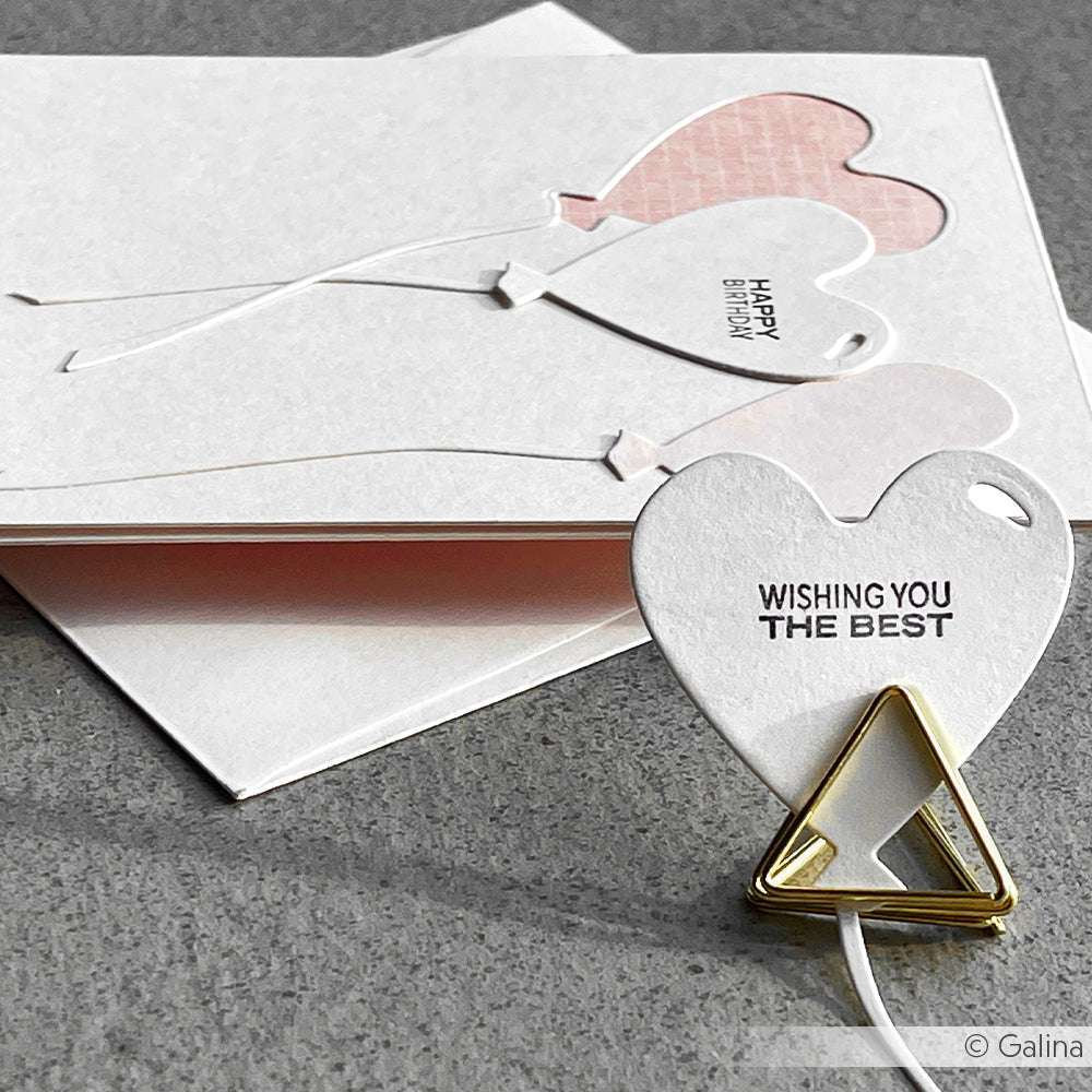 Auf den herzförmigen Papierkarten, die mit den Photopolymer-Stempeln von Alexandra Renke hergestellt wurden, stehen Botschaften wie WISHING YOU THE BEST und HAPPY BIRTHDAY auf einer grauen Oberfläche.