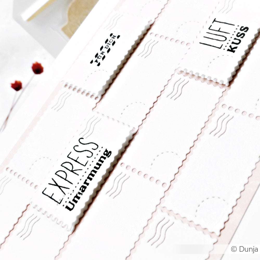 Nahaufnahme der dekorativen Alexandra Renke-Papiermarken, die Photopolymer-Stempel mit deutschen Wörtern wie EXPRESS Umarmung und LUFT KUSS auf einer weißen Fläche zeigen.