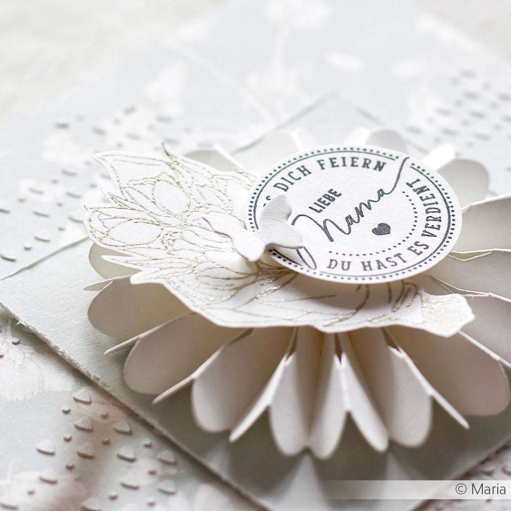 Eine weiße, handgefertigte Blumenkarte von Alexandra Renke mit einem runden "Blumen für dich"-Etikett in deutscher Sprache und zarten Papierdetails, die mit einem Klarsichtstempel für gestochen scharfe Abdrücke hergestellt wurden.