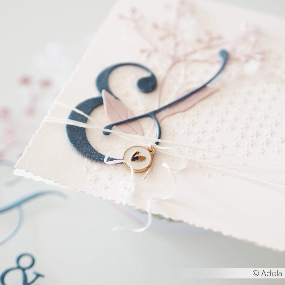Nahaufnahme einer eleganten Hochzeitseinladung mit marineblauem Ampersand, Herzanhänger und zarten Blumendetails, hergestellt mit Alexandra Renke Motivstanze Und-Zeichen und hochwertigen Designpapieren.